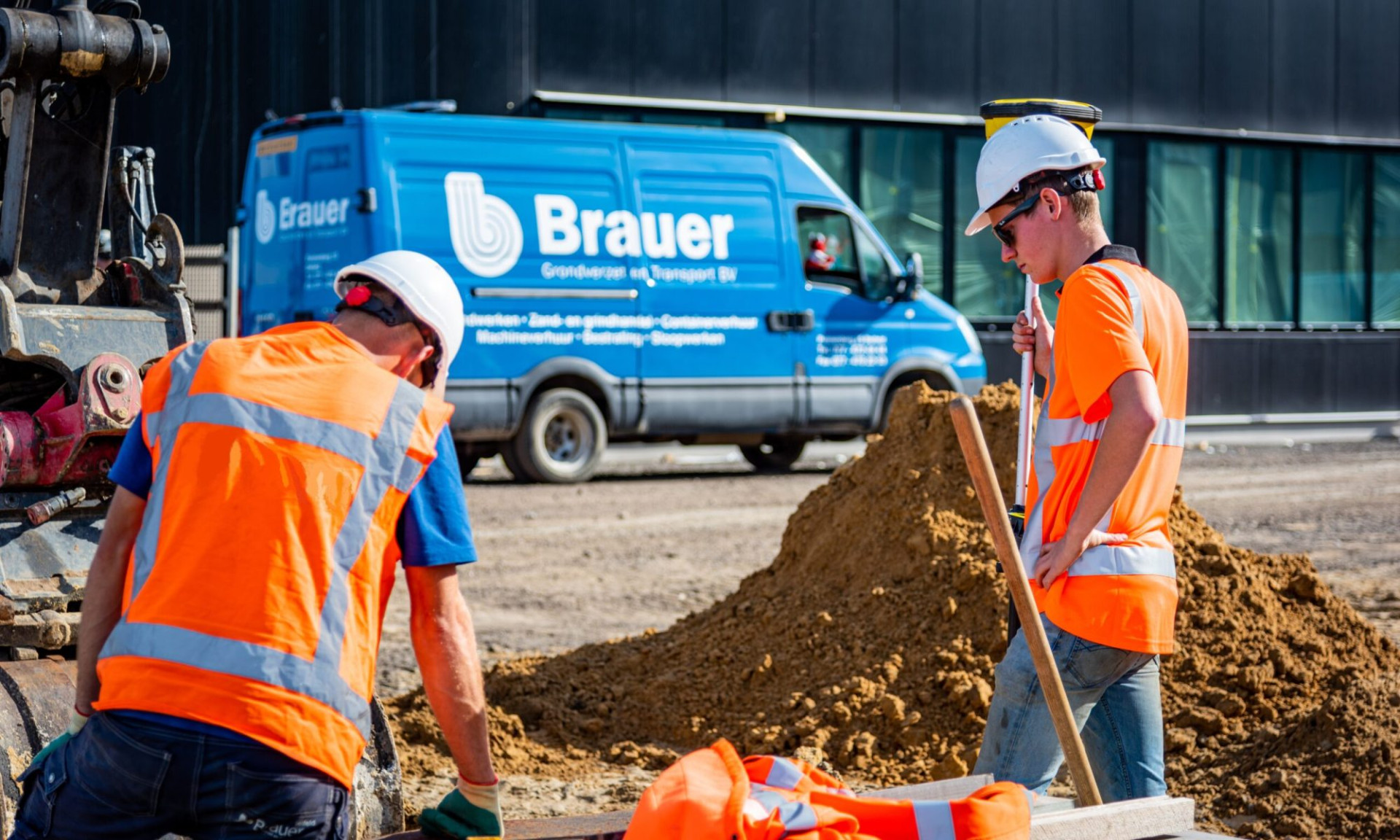 2 werknemers met oranje veiligheidsvest op een bouw plaats met werkbus op de achtergrond