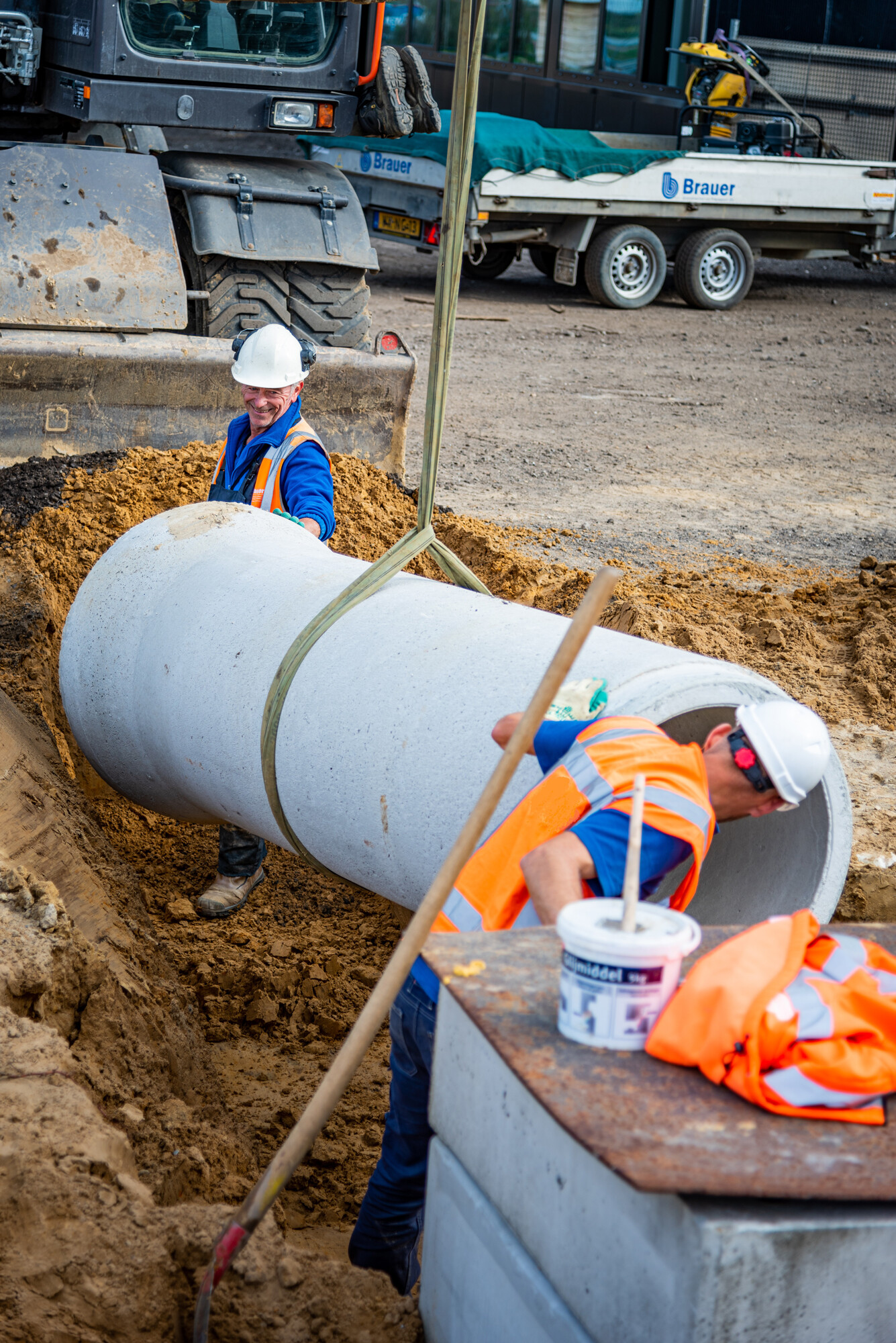 Mannen in oranje veiligheidskleding leggen een rioolbuis in de grond
